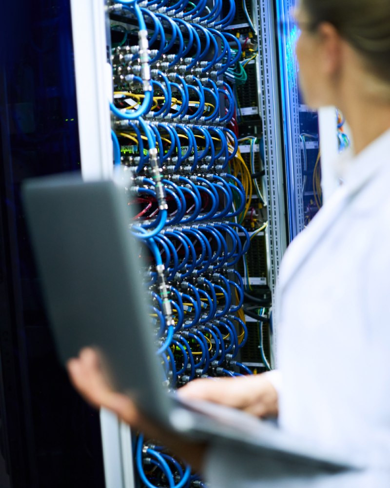 Network engineer managing patch panel cabling with laptop