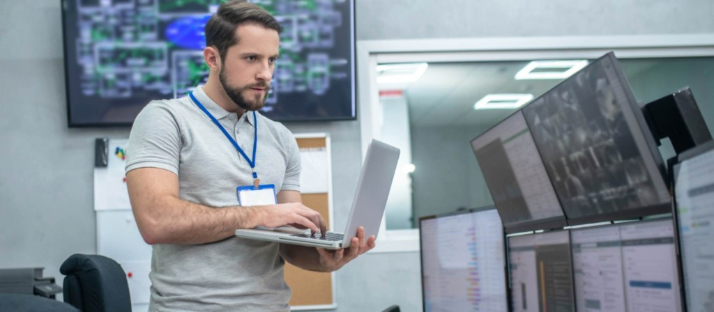 Engineer monitoring system management panel with laptop in monitoring room