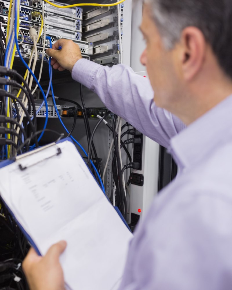 System maintenance technician performing server cabinet check with clipboard